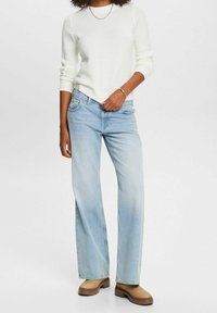 Jean en denim bleu clair avec une coupe décontractée et une jambe droite, associé à un pull en tricot texturé blanc et des chaussures brunes.