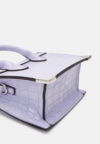 Lavendel håndtaske med krokodillemønster og sorte kanter, sølv hjørnebeskyttere, to runde hanke og en sidelås på en hvid baggrund.