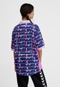 Camisa de manga curta em azul e rosa, com padrões geométricos. Inclui um colarinho branco e texto "INTERNATIONALS" nas costas.