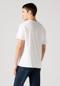 Witte katoenen T-shirt met een ronde hals en korte mouwen, met een rechte snit en minimale stikdetails, gedragen met donkerblauwe jeans.