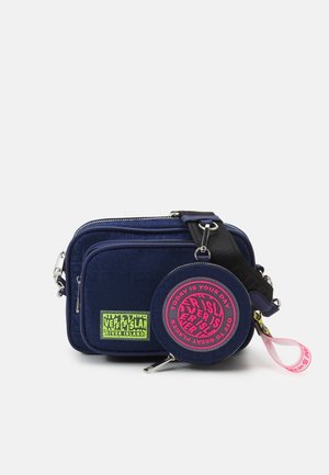 Mørkeblå crossbody-taske med lynlåslomme foran, tilhørende rund møntlomme med pink tekst, sort justerbar rem og grønt River Island-logo patch.