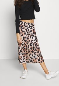 Hame midi satin bercorak macan tutul dengan kilau lembut, menampilkan siluet yang mengalir. Dipadukan dengan atasan hitam bergaris lengan panjang dan sepatu sneakers putih.