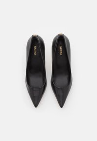 Escarpins noirs en cuir à talons hauts avec un design à bout pointu, texture lisse et logo doré "GUESS" sur la voûte interne.
