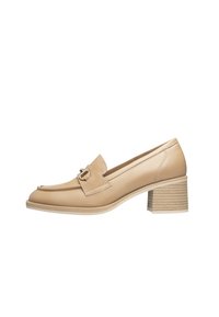 Beige lederen loafers met blokhak en een ronde neus, voorzien van een decoratieve riem en gesp, en een getextureerde lichttan hak.