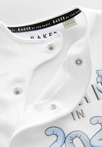 Fehér pamut rugdalózó gombos záródással a nyaknál, "BAKER by TED BAKER" címkével és színes grafikai nyomattal az elején.