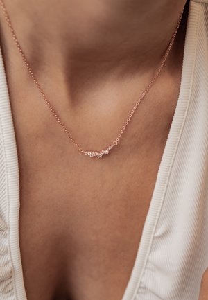 Delicate rose gold chain necklace with small clustered clear gemstones resting on a person's upper chest and neck.