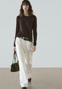Brown long-sleeve top paired with white wide-leg pants, a black belt, and a dark bag. Smooth fabrics with a simple, casual design.