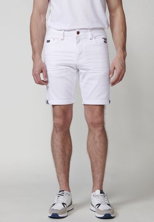 Pantalones cortos de mezclilla blanca con puños enrollados, que presentan un cierre frontal con botón, dos bolsillos laterales y un pequeño parche con el logo en la cadera izquierda.
