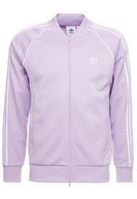 Lila Adidas zip-up jacka med vita dekorationsstripes på ärmarna, ribbade muddar och krage. Har sidofickor och klassisk logotyp på bröstet.