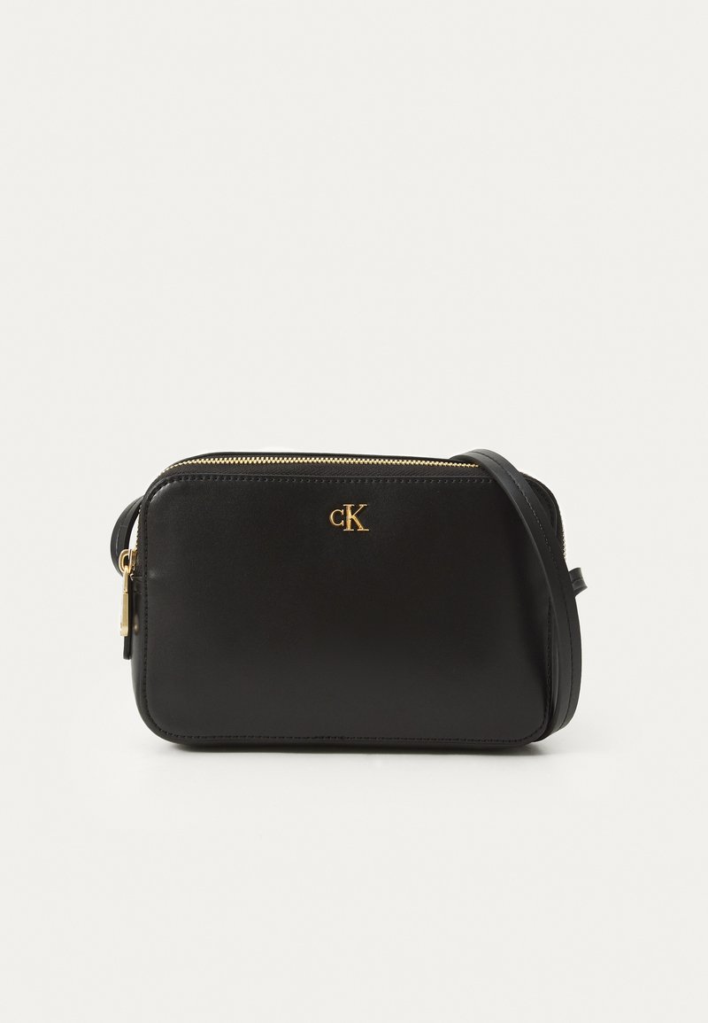 Schwarze Leder-Umhängetasche mit goldenem Reißverschluss, geprägtem "CK"-Logo und einfacher rechteckiger Form. Verstellbarer Schultergurt ist enthalten.