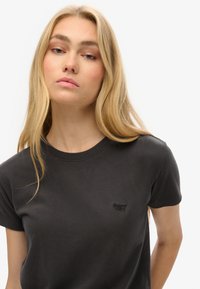 T-shirt in cotone nero con collo rotondo e maniche corte; presenta un logo ricamato discreto sul petto. Texture morbida.