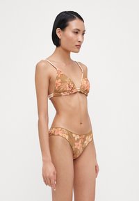 Blomstertrykt bikini-sett i jordfarger, med trekantsbralette med tynne stropper og matchende lavtsittende bunn med blomsterdetaljer.