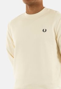 Felpa color crema realizzata in tessuto morbido, con collo rotondo e un piccolo logo ricamato in nero sul petto.