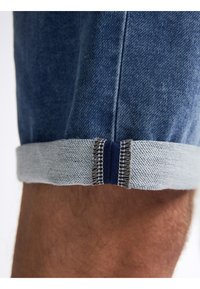 Shorts in denim blu scuro con risvolto in blu chiaro, caratterizzati da cuciture a contrasto e un bordo piegato, che mettono in evidenza texture e dettagli di design.