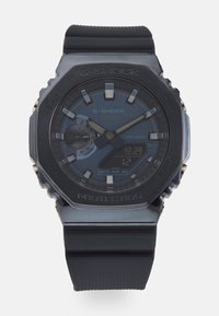 Ceas G-SHOCK cu brățară din cauciuc negru, carcasă octogonală, cadran gri, accente argintii, afișaj digital și rezistență la apă de până la 20 de bari.