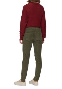 Roter gerippter Pullover mit lockerer Passform, kombiniert mit olivgrünen Cordhosen mit Gesäßtaschen und schmalem Bein. Trägt weiße Sneakers.