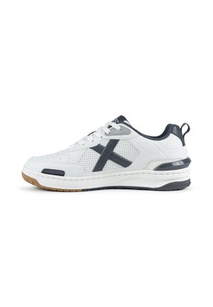 Scarpa da ginnastica bianca e nera con lati traforati, chiusura frontale con lacci e suola color gomma, mostrata di profilo su sfondo bianco.