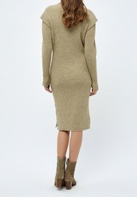Abito midi lavorato a maglia in verde oliva, con texture a coste, dettagli sulle spalle e spacchi laterali. Abbinato a stivaletti beige con tacco altura alla caviglia.