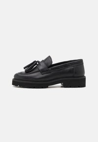 Svarta läderloafers med en platt, texturerad sula, dekorativa fransar framtill och en stilren, minimalistisk design.