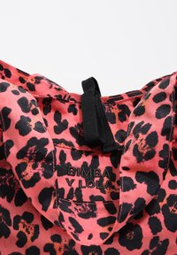 Zbliżenie na różowo-czarny materiał w panterkę z czarnym, wyszywanym logo "BIMBA Y LOLA" oraz czarną pętlą z materiału.