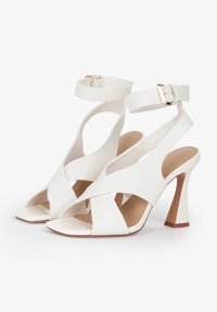 Sandali con tacco alto bianchi, open-toe, con cinturini incrociati, fibbia alla caviglia, soletta testurizzata e tacco triangolare. Materiale sintetico liscio.