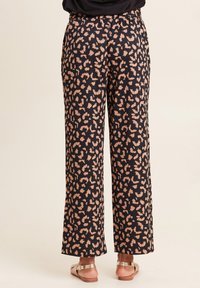 Zwarte pantalons met een luipaardprint in gedempte beigetinten, met een ontspannen pasvorm en een elastische tailleband. Platte sandalen zichtbaar.