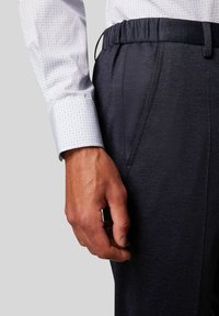 Marineblauwe geprinte broek met een elastische tailleband, gecombineerd met een lichtblauw shirt met een klein geometrisch patroon.