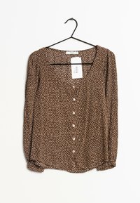 Blusa marrón con lunares blancos, de manga larga, escote en V, cierre frontal con botones y una tela suave y ligera. Etiqueta adjunta en exhibición.
