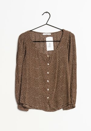 Braune Bluse mit weißen Punkten, langen Ärmeln, V-Ausschnitt, Knopfverschluss vorne und aus einem weichen, leichten Stoff. Etikett ist zur Schau gestellt.