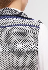 Gilet lavorato a maglia con un motivo testurizzato in nero, bianco e blu. Presenta un colletto alto e dettagli di intreccio intricati.