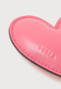 Ροζ δερμάτινη λεπτομέρεια σε σχήμα καρδιάς με λείο υφή, που διαθέτει μαύρα ραφές και ανάγλυφο λογότυπο.