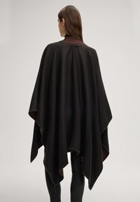 Zwarte wollen poncho met een hoge hals, featuring een losse pasvorm, asymmetrische zoom en contrasterende stiksels langs de randen.