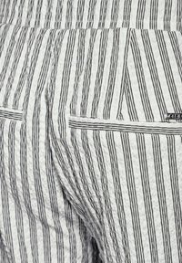 Striped fabric trousers in white and black, featuring a textured surface and two back pockets with horizontal detailing.