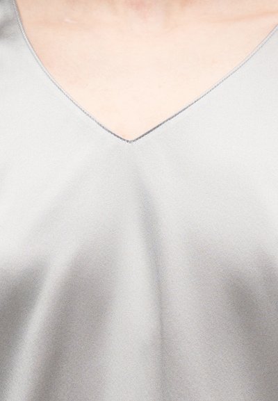 Gros plan sur un vêtement en satin gris clair avec un décolleté en V sur une peau nue.