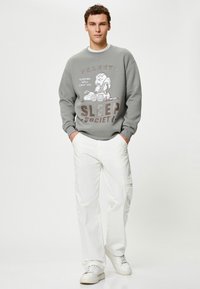 Szary sweatshirt z grafiką "Peanuts Sleep Society", przedstawiający Snoopy. Połączony z białymi spodniami cargo, które prezentują luźny krój i kieszenie.