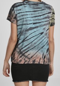 Tie-dye t-shirt med korta ärmar; har mönster i blått, svart och persika. Tillverkad av bomull med en avslappnad passform och rundad halsringning.