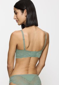 Sosten verde de encaje con borde en forma de ondas, tirantes ajustables y cierre en la espalda con gancho y ojo; combinado con braguitas de encaje y tela a juego.