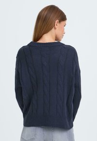 Pullover lavorato a maglia blu navy con motivo a treccia, orlo a coste e scollatura rotonda, mostrato dal retro. Tessuto morbido.