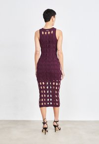 Robe tricotée bordeaux avec une silhouette ajustée, présentant des motifs découpés et une longueur mi-mollet. Modèle sans manches avec un col rond.