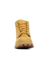 Bota de cuero marrón con ojales de metal y cordones amarillos. Punta redonda, cuello acolchado y suela de goma texturizada con surcos profundos.