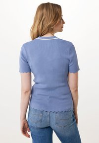 Ljusblå ribbade kortärmade topp med vågiga kanter, försedda med en vit krage, bärs tillsammans med ljus tvättade jeans.