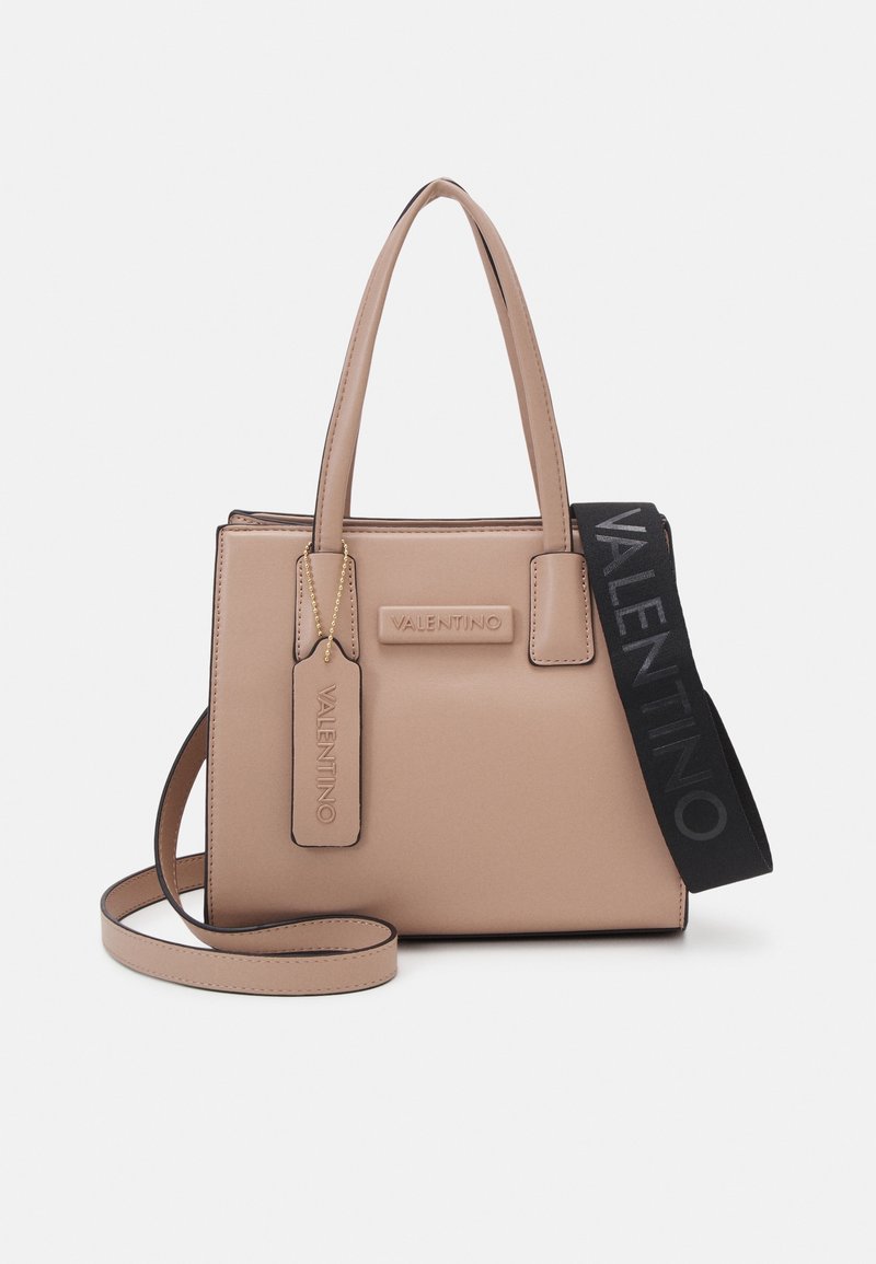 Tan leather handbag with structured design, short handles, and removable black strap. Features embossed branding and a small tag.