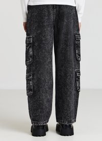 Pantaloni cargo in denim nero con una texture sbiadita, dotati di due tasche laterali e una vestibilità ampia, abbinati a stivali neri chunky.