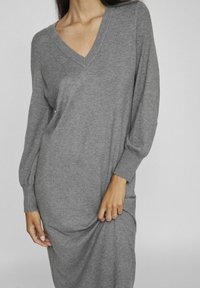 Abito grigio lavorato a maglia con scollo a V e maniche lunghe a palloncino, caratterizzato da una vestibilità rilassata che si adagia delicatamente sul corpo.