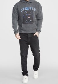 Felpa grigia con grafica di un pantera, modello a pullover, con tasca frontale e polsini a costine, abbinata a jeans neri e sneakers bianche.