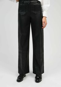 Pantalon en cuir noir avec une coupe droite, doté de deux poches avant et d'une texture lisse. Assorti à des chaussures en vernis.