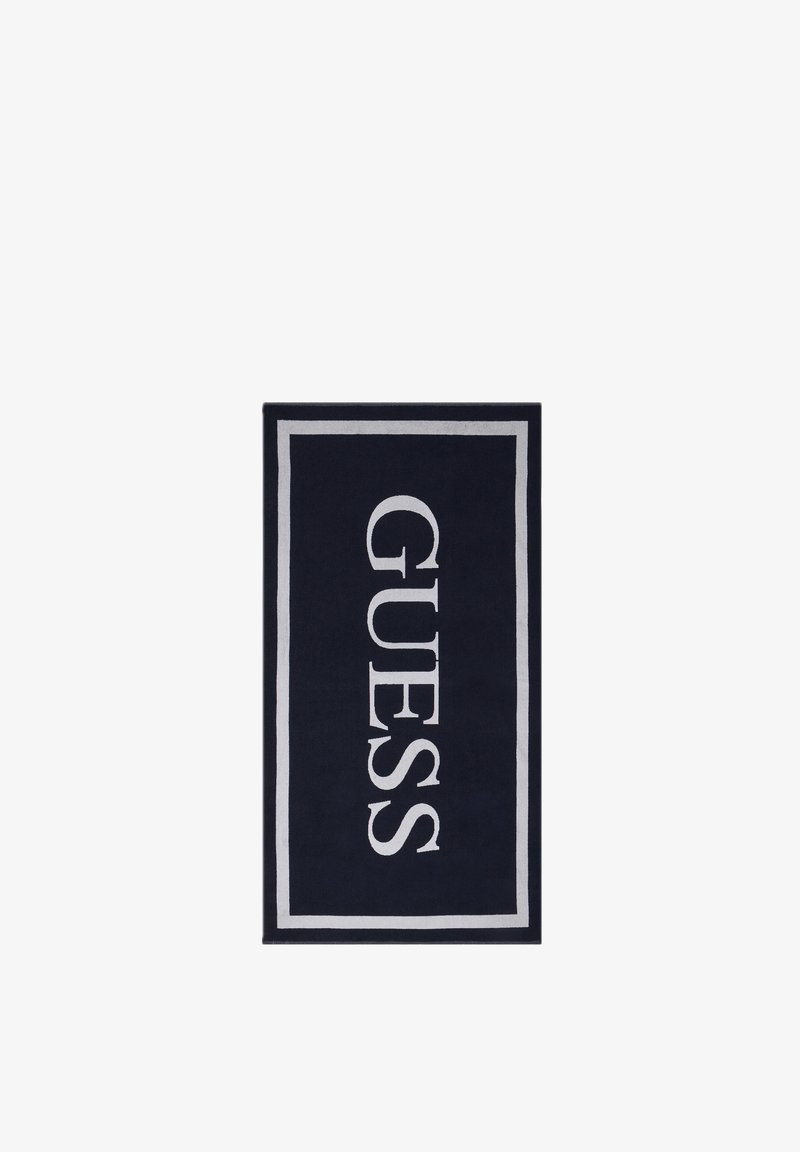 Serviette rectangulaire noire avec une bordure blanche et "GUESS" écrit verticalement en grandes lettres blanches au centre.
