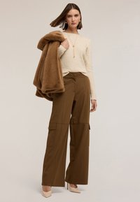 Brązowe, szerokie spodnie cargo z bocznymi kieszeniami i guzikami, w połączeniu z kremowym, teksturowanym swetrem oraz miękką, brązową futrzaną kurtką.
