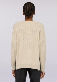 Maglione beige lavorato a maglia con motivi a coste e a trecce, vestibilità oversize, scollo rotondo e orlo posteriore leggermente più lungo. Tessuto di trama.