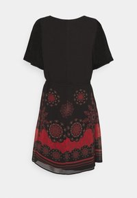 Robe noire à manches courtes avec des motifs floraux rouges et noirs sur la jupe et une taille cintrée, vue de dos.